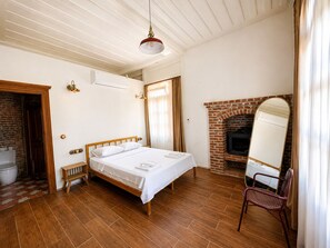 A bedroom with a wooden bed, a brick fireplace, and a mirror. - Konak 1882 (Ayvalik)