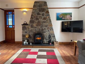 Ein Wohnzimmer mit Kamin aus Stein, einer Holztür mit Buntglasfenstern, einem Flachbildfernseher und einem Schachbrettteppich.