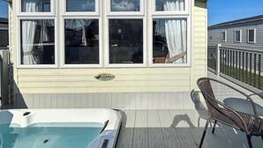 A covered outdoor area with a hot tub, a deck, and a building with multiple windows. - Sunnymede B8 - UKC9571 (Ingoldmells)