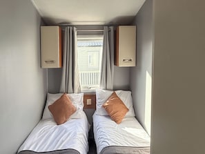 Ein kleiner, kompakter Raum mit zwei Einzelbetten, einem fensterbelaubten Fenster und fest eingebauten Schränken.