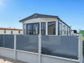 Ein modernes Mobilheim mit Garage, großen Fenstern und umzäunter Außenbereich.