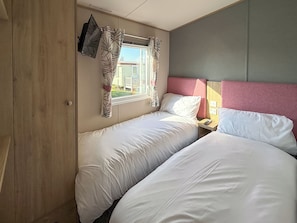 Quarto com duas camas, janela com cortinas, mesa de cabeceira e cabeceira.