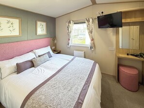 A bedroom with a bed, a television, a window with curtains, a radiator, and artwork on the wall.