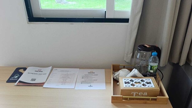 Ein Holztisch mit Stuhl, ein Fenster mit Blick ins Grüne und ein Tablett mit einer Teedose und einer Flasche.