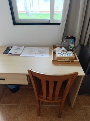 A wooden desk with a chair, a window with a view of greenery, and a tray with a tea box and a bottle. - Casa Erica (Soyo)