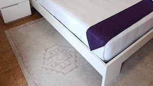 Ein ordentlich bezogenes Bett mit weißer Bettwäsche, einer violetten Tagesdecke und passendem Kopfteil.