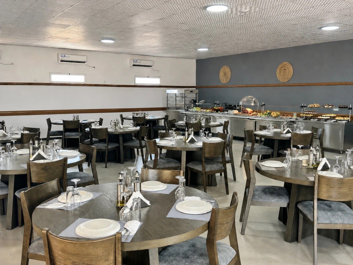 A dining area with round tables, chairs, and a buffet line with various food items.