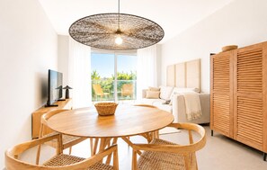 Ein modernes Wohnzimmer mit einem runden Holzesstisch, Korbstühlen, einer gewebten Pendelleuchte, einer Couch und einem Holzkabinett.