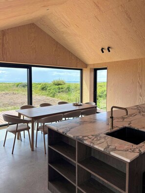 A modern kitchen with a marble countertop, a sink, and a dining area with chairs. - Nordic summer house with view over Storebælt (Slagelse)