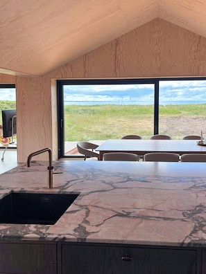 A modern kitchen with a marble countertop, a sink, and a view of a grassy field and bridge. - Nordic summer house with view over Storebælt (Slagelse)