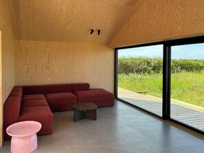 A modern interior with a wooden ceiling, a red sectional sofa, a small table, and a pink stool. - Nordic summer house with view over Storebælt (Slagelse)