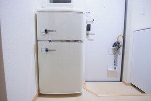 Ein weißer Kühlschrank steht in einer Ecke des Raumes, mit einer Tür und einem kleinen Regal mit einem Regenschirm.