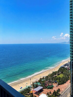 Vista da praia com céu claro, areia dourada e um edifício alto em primeiro plano.