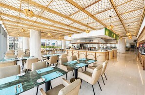 Um restaurante moderno com teto alto, mesas, cadeiras e uma área central de cozinha.
