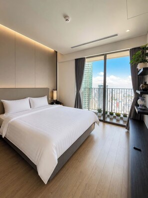 Quarto de hotel moderno com uma cama grande, uma mesa de cabeceira, uma janela com vista para a cidade e uma varanda com plantas em vasos.