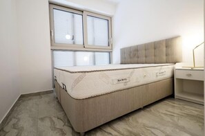 Ein Schlafzimmer mit Bett, Fenster mit Jalousien, Nachttisch und Lampe.