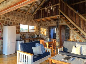 A rustic interior with a stone wall, wooden beams, a kitchen area, and two sofas.