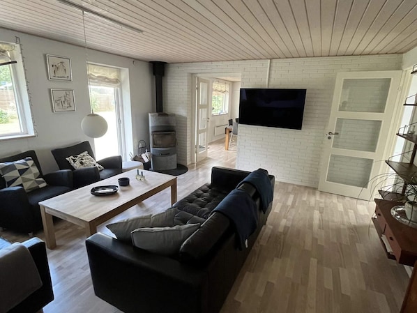 A modern living room with a fireplace, a flat-screen TV, a sofa, and a dining table. - 5 Star Holiday Home in Vaeggerlose (Vaeggerlose)