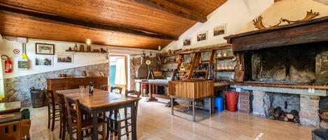 A rustic kitchen with wooden beams, a stone wall, and a fireplace.