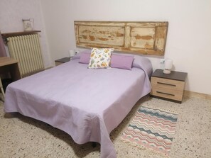 Un dormitorio con cama, mesitas de noche, un radiador y una alfombra estampada.