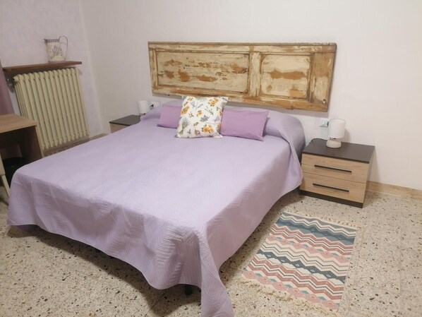 A bedroom with a bed, nightstands, a radiator, and a patterned rug.