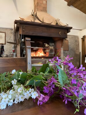 Ein rustikaler Kamin mit Geweihen, ein Holztisch mit Blumen und eine Ziegelwand.