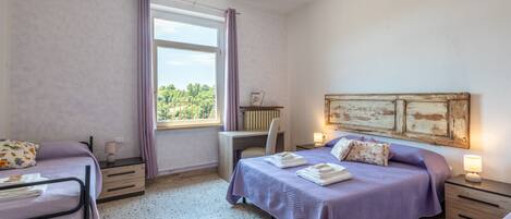 A bedroom with two beds, a desk, a chair, and a window with curtains.