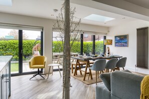 Uma zona de refeições moderna com uma mesa posta para quatro pessoas, uma cadeira amarela e um sofá cinzento.