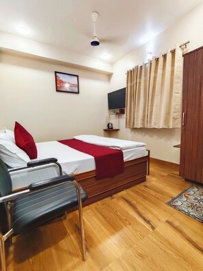 A bedroom with two single beds, a chair, a television, and a wardrobe. - Serenitysteay (Varanasi)