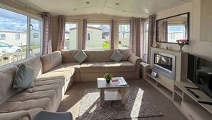 Una sala de estar acogedora con un sofá modular, un televisor de pantalla plana, una chimenea y ventanas amplias con vistas al vecindario.