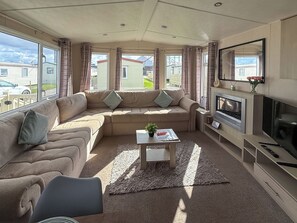 Ein gemütliches Wohnzimmer mit einer Eckcouch, einem Flachbildfernseher, einem Kamin und großen Fenstern mit Blick auf die Nachbarschaft.