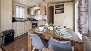 Una cocina compacta con armarios de madera, una mesa de comedor preparada para cuatro personas y un ventanal con cortinas.