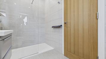 Un baño moderno con cabina de ducha de vidrio, una puerta de madera y un lavamanos blanco.
