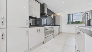 A modern kitchen with white cabinetry, stainless steel appliances, and a large window offering a view of greenery. - Oakwood House (Matlock)
