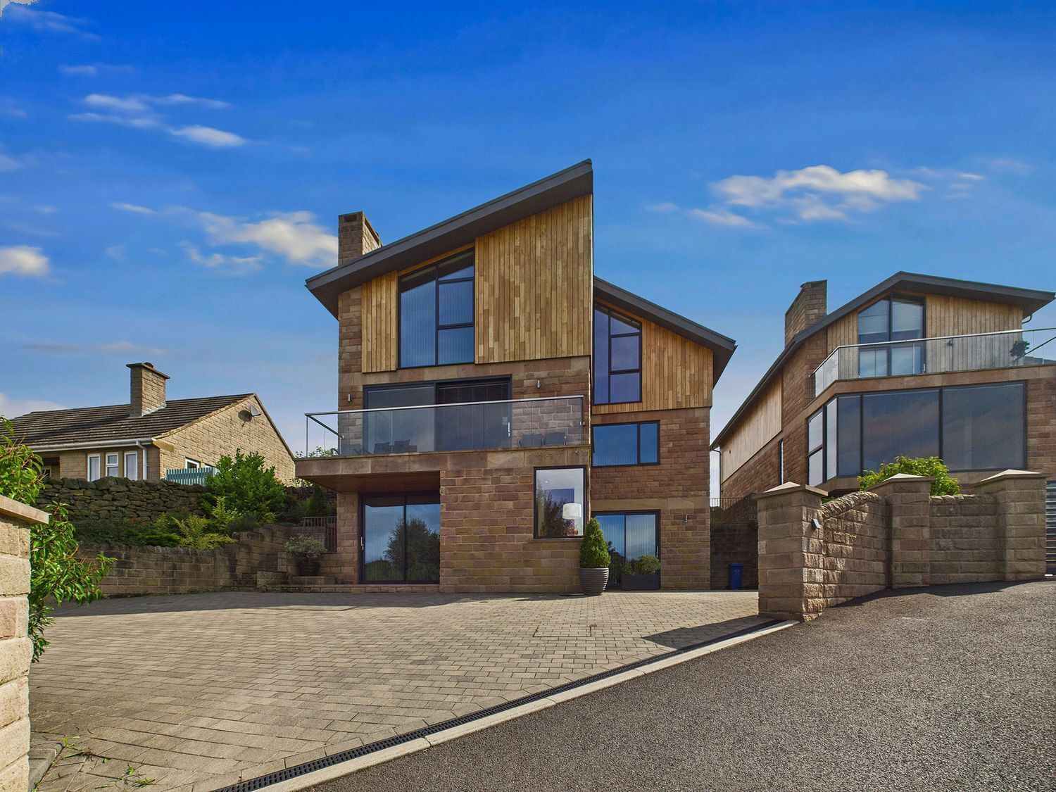 A modern two-story house with a stone facade, large windows, and a paved driveway.