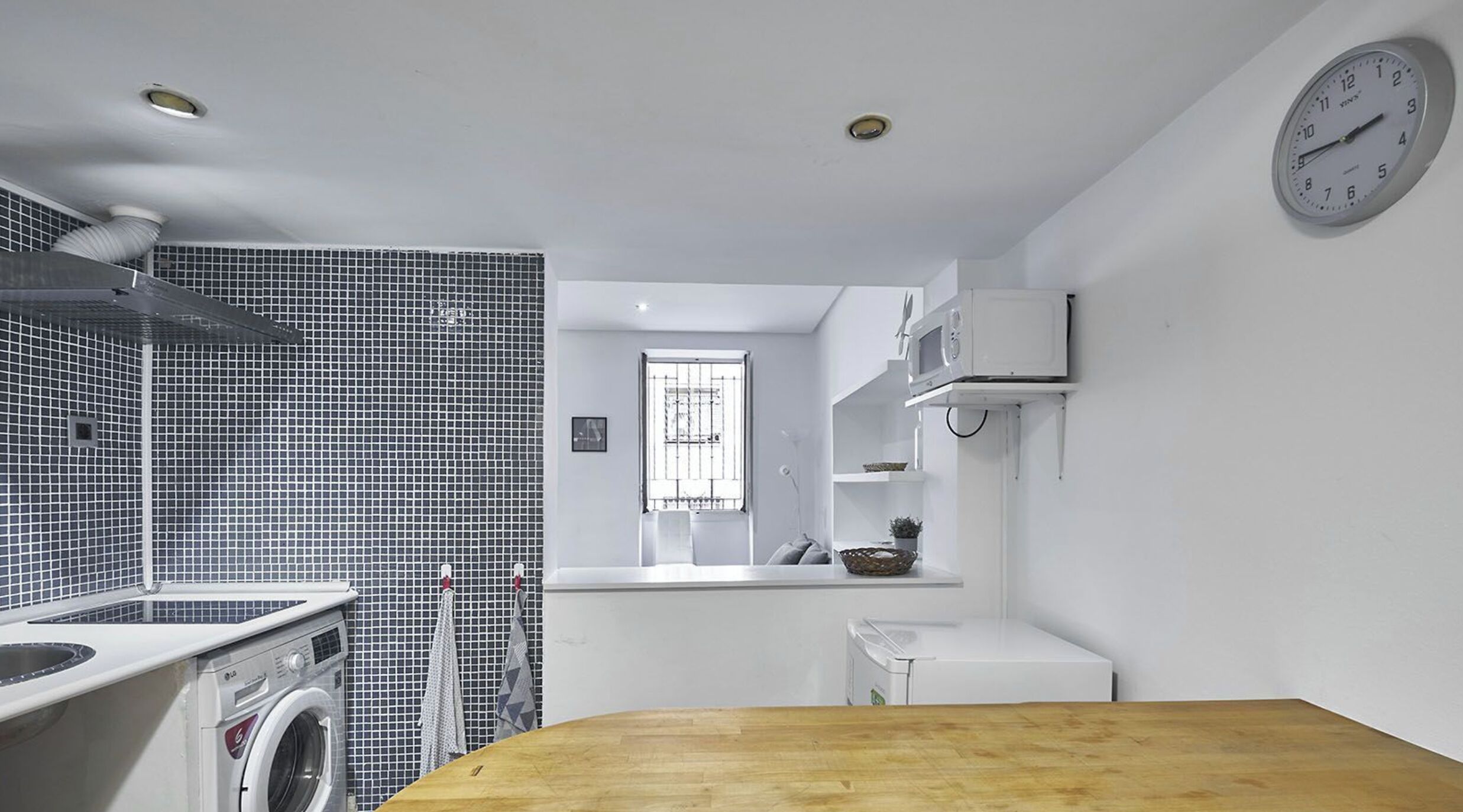 A compact kitchen with a washing machine, a microwave, and a wooden table.