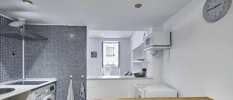 A compact kitchen with a washing machine, a microwave, and a wooden table.