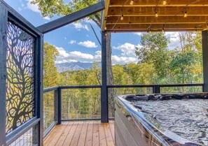 Ein Whirlpool auf einer Holzterrasse mit Blick auf Bäume und Berge.
