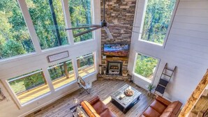 A spacious living area with a stone fireplace, large windows, and a ceiling fan. - Mt LeConte Views • 3 Kings • Sleeps 12 • Hot Tub (Gatlinburg)