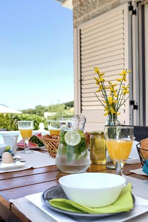 Una mesa dispuesta con alimentos para el desayuno, una jarra de limonada y un florero con flores amarillas.