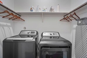 A laundry room with two front-loading washing machines and a shelf above containing cleaning products. - NRG Access | Sleeps 10 | Near The Heights (Houston)