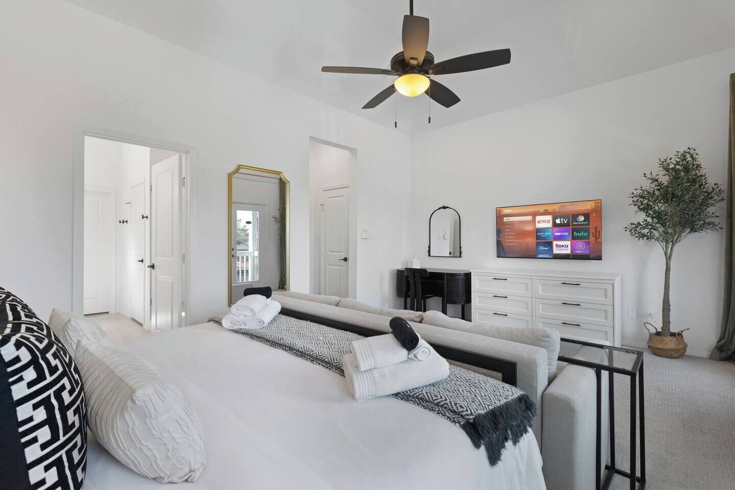 Ett modernt hotellrum med en stor säng, ett skrivbord, en stol, en TV och en takfläkt.