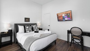 A neatly arranged hotel room with a bed, bedside tables, a chair, and a wall-mounted TV displaying streaming services. - NRG Access | Sleeps 10 | Near The Heights (Houston)