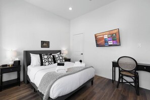 A neatly arranged hotel room with a bed, bedside tables, a chair, and a wall-mounted TV displaying streaming services. - NRG Access | Sleeps 10 | Near The Heights (Houston)