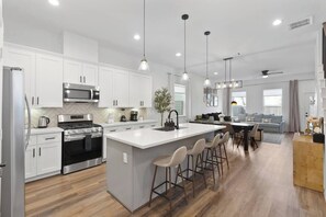 A modern kitchen with white cabinets, stainless steel appliances, a central island with bar stools, and pendant lighting. - NRG Access | Sleeps 10 | Near The Heights (Houston)