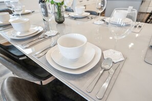 Ein Esstisch, festlich gedeckt mit weißen Tellern, Schüsseln, Besteck und Gläsern, was auf eine formelle Tafel hinweist.