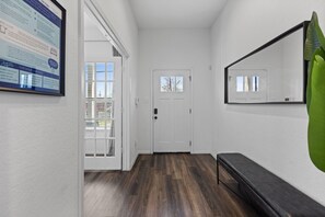 Ein Flur mit Holzboden, einer weißen Tür, einer Bank und einem an der Wand befestigten Informationsplakat.