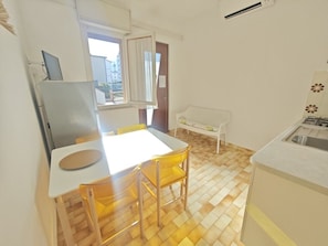 A compact kitchen with a dining area, a bench, and a window. - Comfortable stay near beach (Lignano Sabbiadoro)