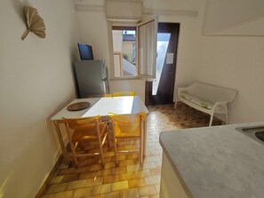 Eine kleine Küche mit Esstisch, Stühlen, einem Kühlschrank und einem kleinen Fenster.