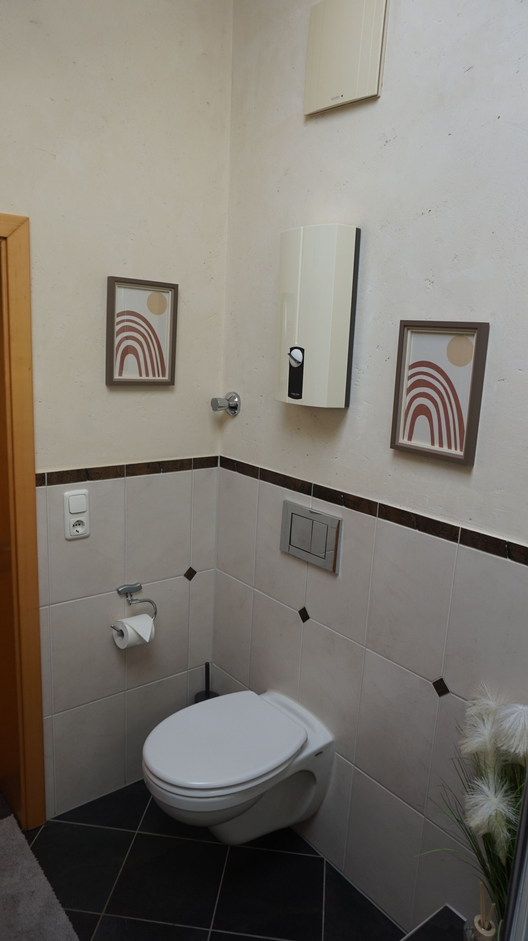 A bathroom with a toilet, a towel dispenser, a mirror, and framed artwork on the wall.